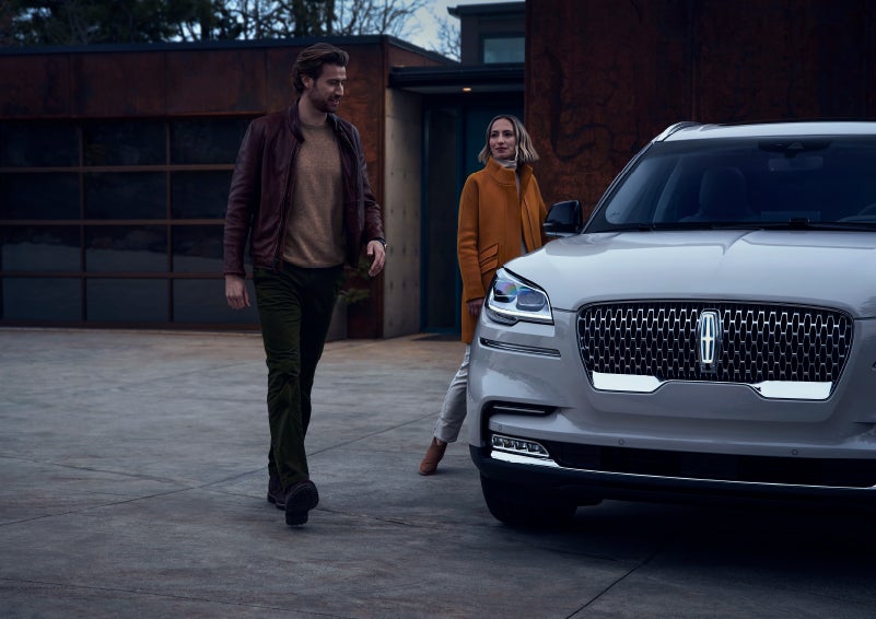 A man and a woman approaching a 2024 Lincoln Aviator® SUV, which illuminates certain lights when they are close | Thornhill Lincoln in Chapmanville WV
