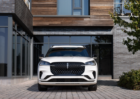 A white 2025 Lincoln Aviator® SUV is shown parked outside a modern building with gray brick and wood accents. | Thornhill Lincoln in Chapmanville WV