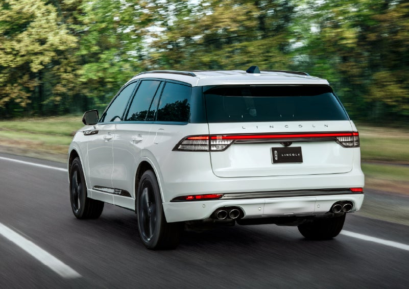A white 2026 Lincoln Aviator® SUV is being driven away down a road lined with colorful trees. | Thornhill Lincoln in Chapmanville WV