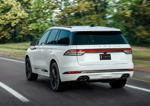 A white 2026 Lincoln Aviator® SUV is being driven away down a road lined with colorful trees. | Thornhill Lincoln in Chapmanville WV