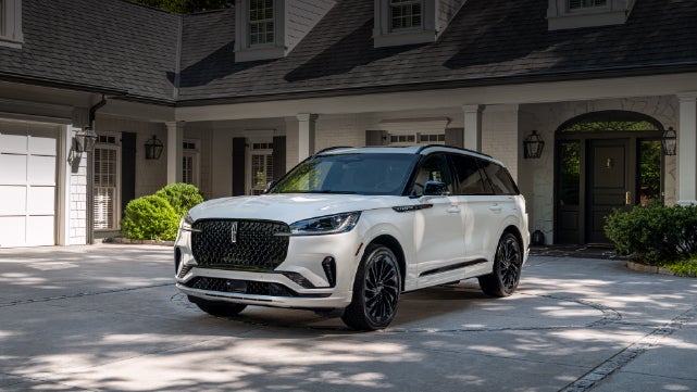 A white 2026 Lincoln Aviator® SUV is parked in the driveway of a luxury home. | Thornhill Lincoln in Chapmanville WV