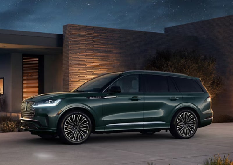 A green 2027 Lincoln Aviator® SUV is parked outside a contemporary home. | Thornhill Lincoln in Chapmanville WV