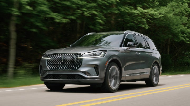A 2027 Lincoln Aviator® SUV is being driven down a road lined with trees. | Thornhill Lincoln in Chapmanville WV